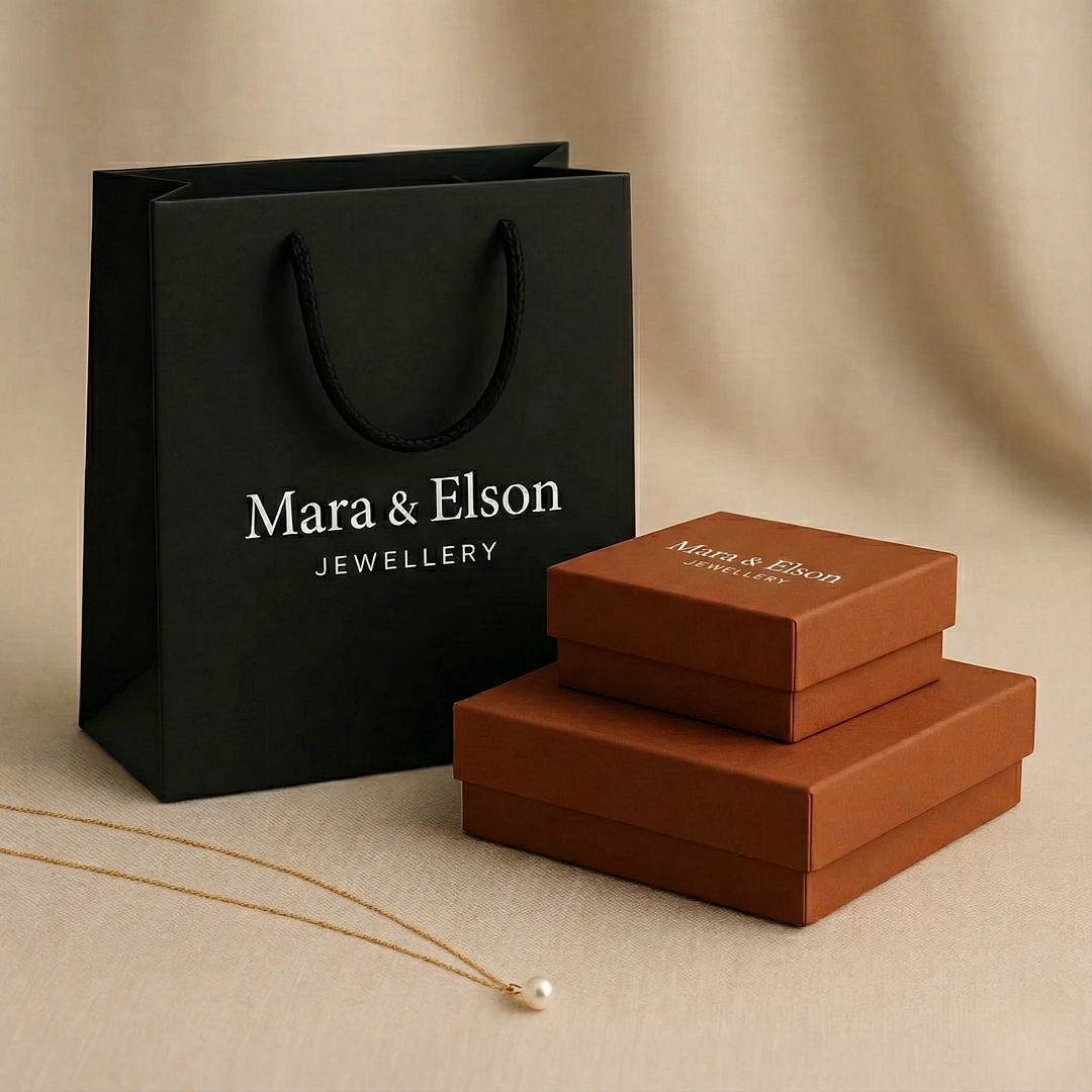 Mara & Elson Jewellery branded black gift bag with stacked terracotta jewelry boxes and a delicate gold necklace with a pearl on a neutral beige background.